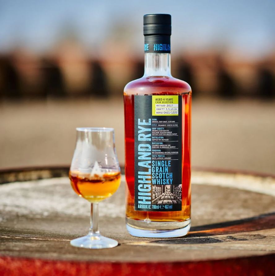A bottle of Arbikie Highland Rye Single Grain Scotch Whisky stands next to a tasting glass on a wooden barrel.
