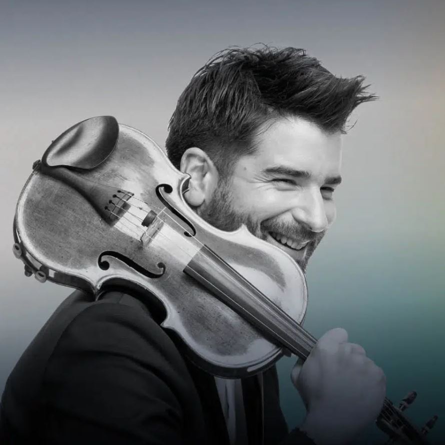 A black-and-white portrait of a smiling man with a beard and dark hair, resting a violin on his shoulder. He is looking off to the side, and the background is a soft, out-of-focus gradient.