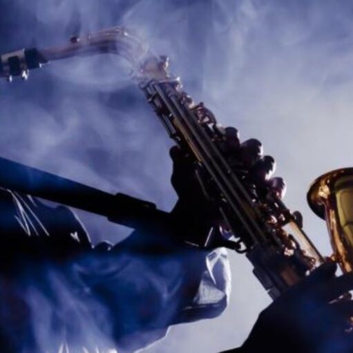 A musician playing a brass saxophone. The musician is silhouetted against a bright, hazy light source, with thick plumes of blue-tinted smoke or fog swirling around them and the instrument, creating an atmospheric, moody jazz club vibe.