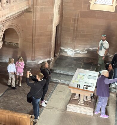 Visitors exploring a large stone hall with architectural carvings and interpretive displays, viewed from an upper gallery.