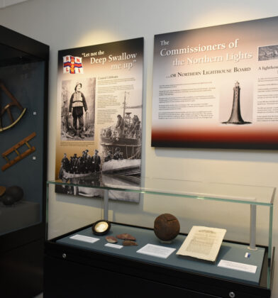 Museum gallery showcasing maritime and lighthouse history, with artefacts displayed in glass cases and large interpretive panels about coastal lifeboats, the Northern Lighthouse Board and the Bell Rock Lighthouse.