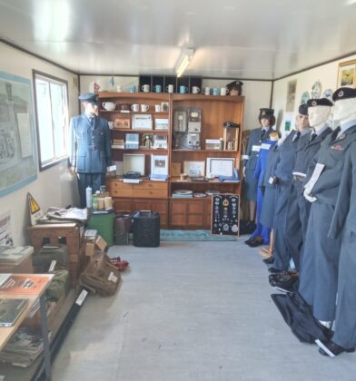 Museum display showcasing Royal Air Force uniforms, equipment, memorabilia and historical artefacts, with mannequins in uniform standing beside display cabinets and interpretive exhibits.
