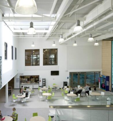 Modern leisure and community hub with a bright open atrium, café seating area and indoor climbing wall, featuring high ceilings, large windows and contemporary design.
