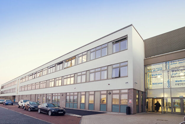Modern multi-storey community campus building with large windows and a contemporary entrance, viewed from the surrounding car park and pedestrian area.