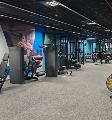 Modern fitness suite featuring cardio machines, free weights, resistance equipment and functional training stations, with mirrored walls and blue accent lighting throughout the spacious gym.
