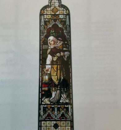 Tall stained-glass panel depicting a robed figure holding a lantern and broom, framed by ornate Gothic-style decorative patterns in red, gold and cream tones.