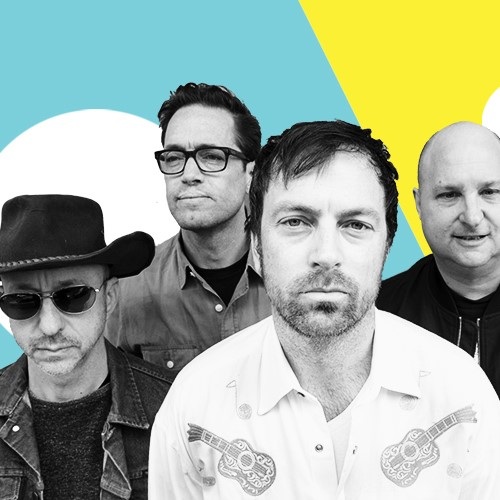 Promotional band photograph featuring four musicians posed against a bold blue, yellow and white graphic background, with one person in a cowboy hat and sunglasses and the others dressed in casual shirts and jackets.