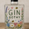 Clear glass bottle decorated with hand-painted floral and nature-themed artwork, displayed on a wooden surface against a neutral background. The bottle has a black cap and features the words “GIN BOTHY” painted in large green lettering across the centre.