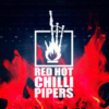 A logo for the band "Red Hot Chilli Pipers" set against a dark stage background framed by bright red flames. The white logo displays a set of bagpipes enveloped in stylized flames inside a square border, with the text "RED HOT CHILLI PIPERS" written in bold capital letters underneath.