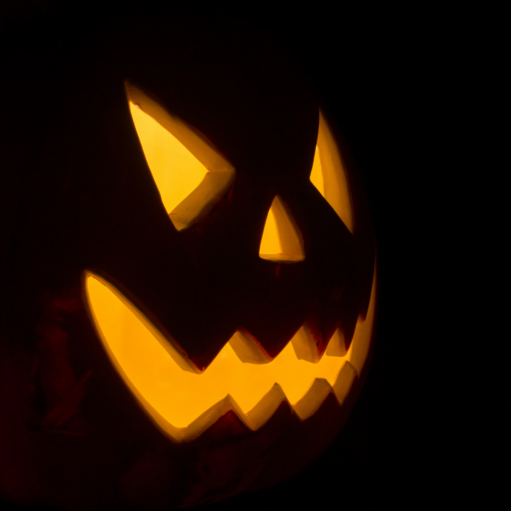 A carved jack-o'-lantern illuminated from within by a warm, yellow glow, showing a menacing face with angled eyes and a jagged smile against a pitch-black background.