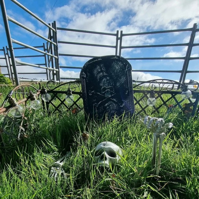A Halloween graveyard display with a skull, skeletal hands, and a tombstone in a grassy field.