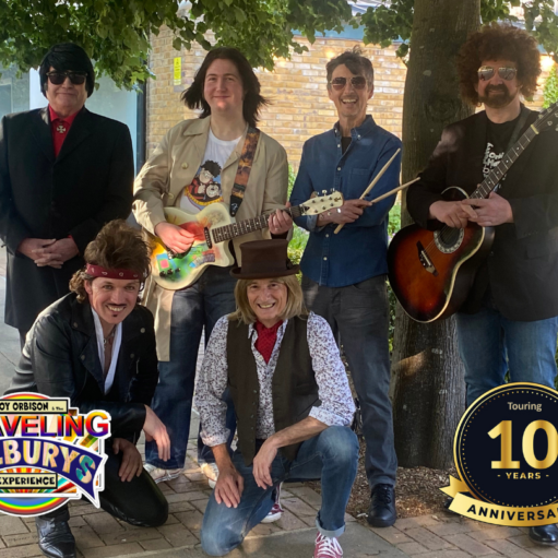 Promotional image for the Roy Orbison and the Traveling Wilburys Experience, featuring six musicians posing outdoors with guitars and performance props beneath a tree. The image includes the show logo and a gold badge highlighting a 10-year anniversary tour.